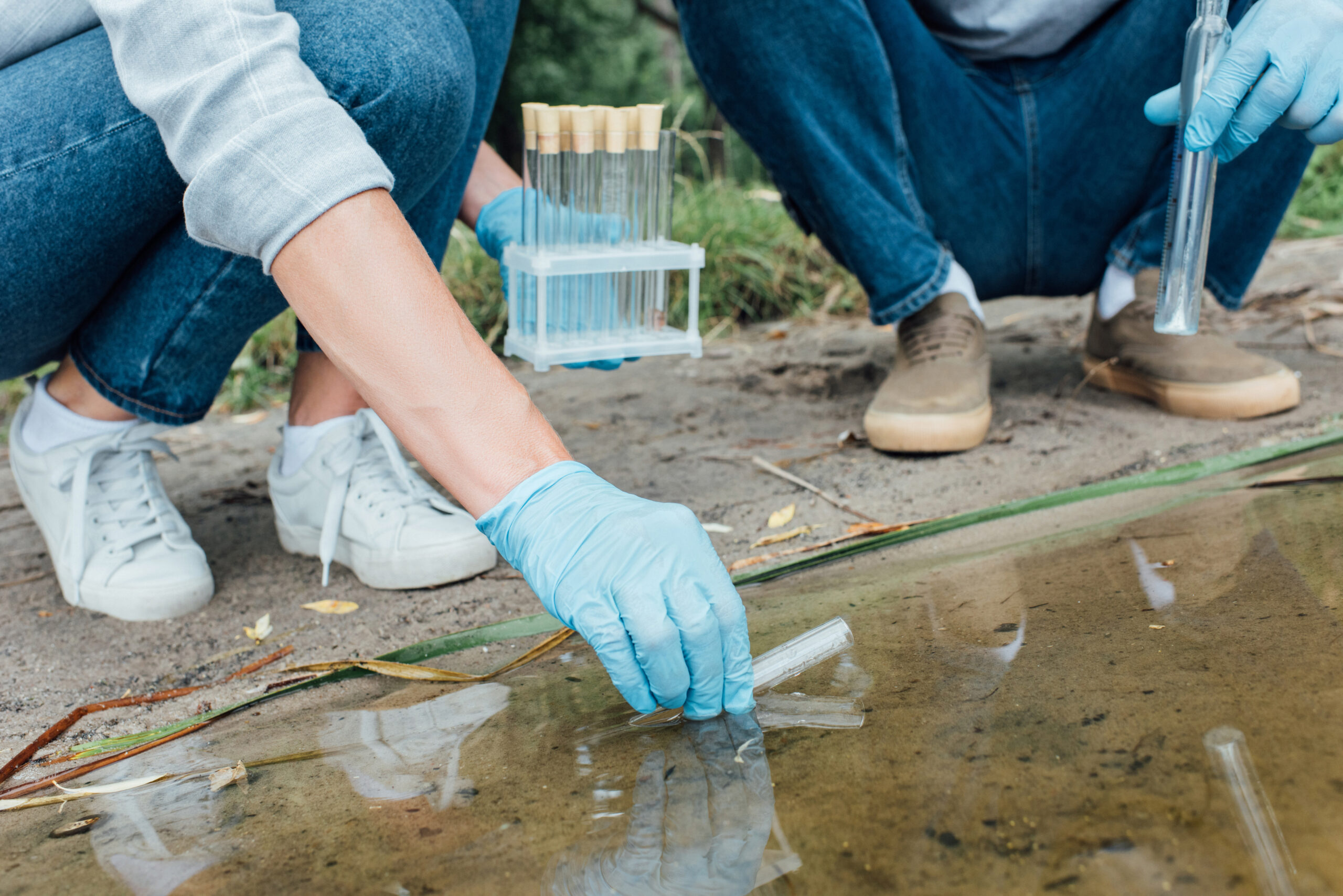 male and female scientists taking sample of water in test flask outdoors
